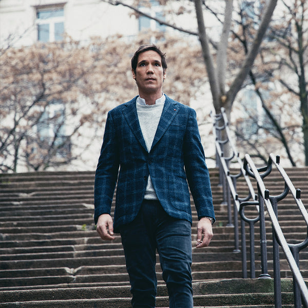 Erwin Creed en un blazer azul bajando unas escaleras exteriores, con un edificio en el fondo.